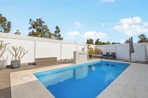 Ein rechteckiger Swimmingpool mit glasklarer, blauer Wasseroberfläche, umgeben von einer weißen Mauer und einer Holzterrasse.