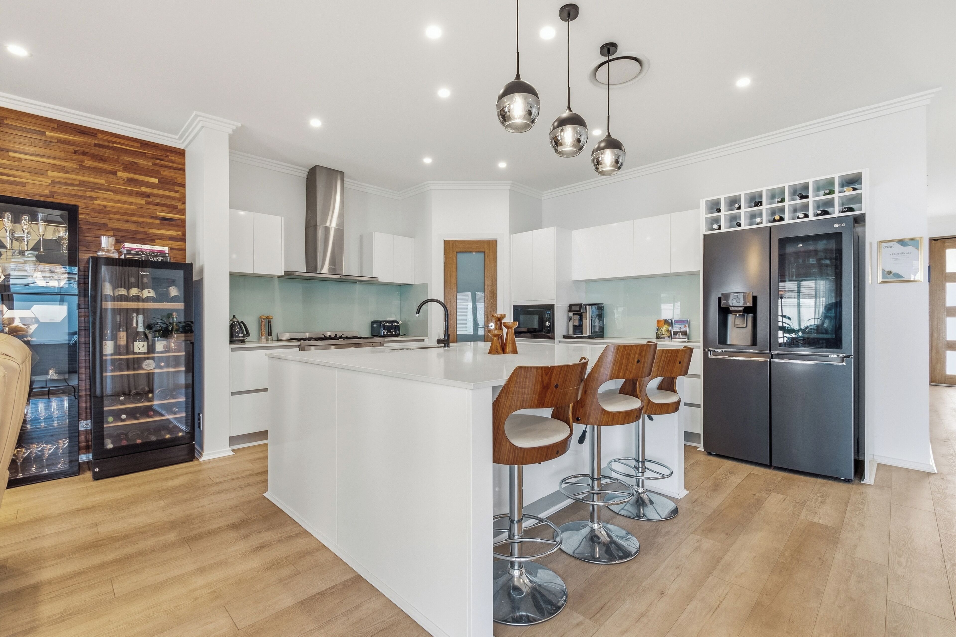 A modern kitchen with a central island, bar stools, a built-in wine fridge, and a double-door refrigerator.