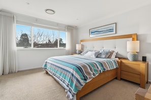 Un dormitorio con una cama grande, dos mesitas de noche, una mesilla, una ventana con cortinas y un cuadro en la pared.