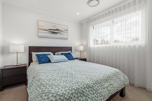 Ein Schlafzimmer mit einem großen Bett, zwei Nachttischen, einem Fenster mit Jalousien und einem Bild an der Wand.
