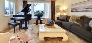A living room with a grand piano, a sofa, a coffee table, and a lamp. - 3-bedroom Charming Farmhouse Near Boyne Mountain (Boyne City)