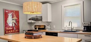 A modern kitchen with a central island, a hanging light fixture, and a large window with blinds. - 3-bedroom Charming Farmhouse Near Boyne Mountain (Boyne City)