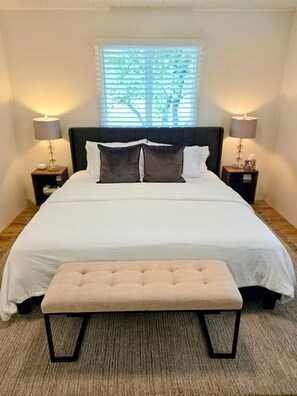A bedroom with a bed, two nightstands, a bench, and a window with blinds. - 3-bedroom Charming Farmhouse Near Boyne Mountain (Boyne City)