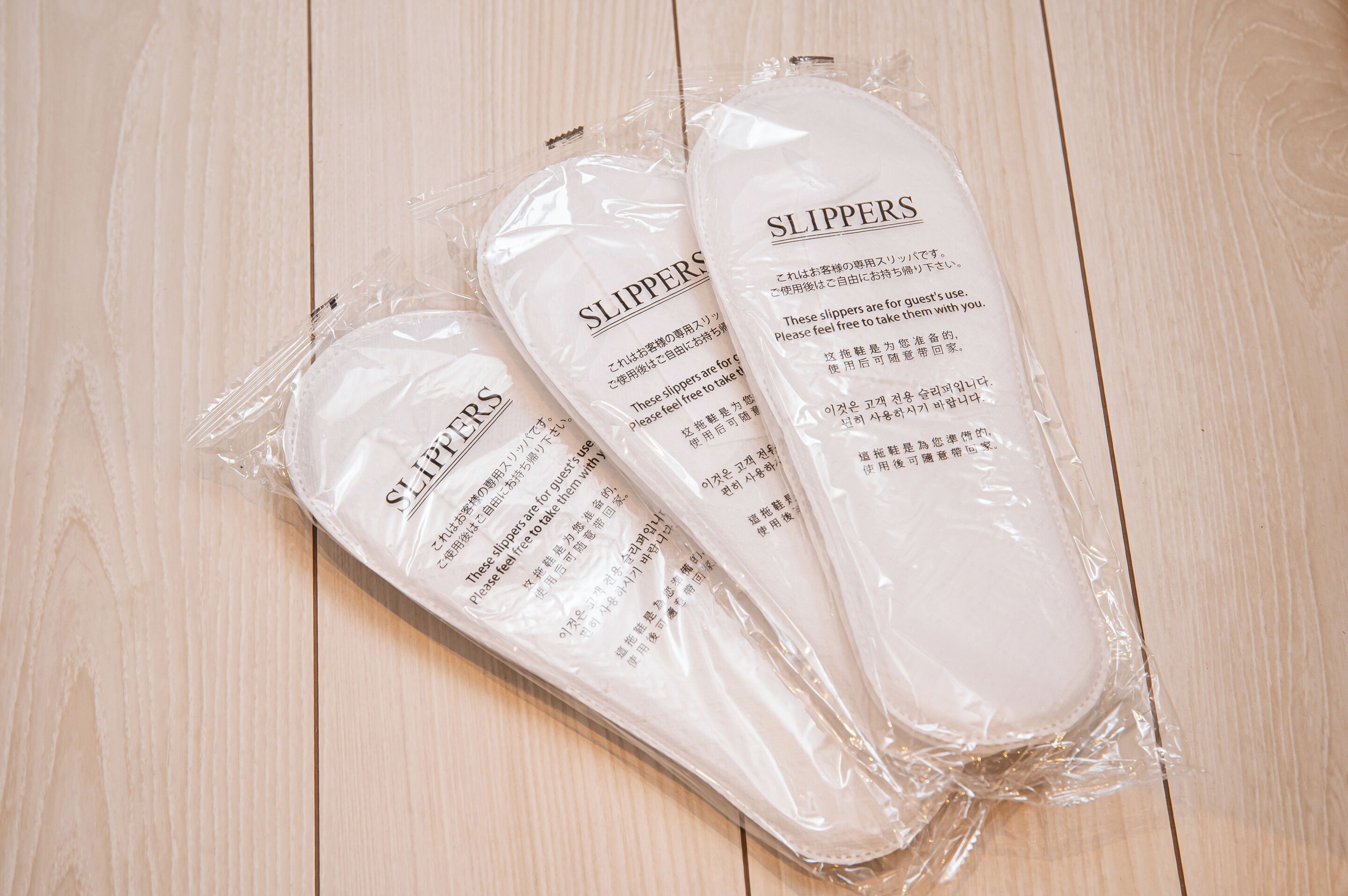 Trois paires de chaussons emballées dans du plastique transparent, posées sur une surface en bois.