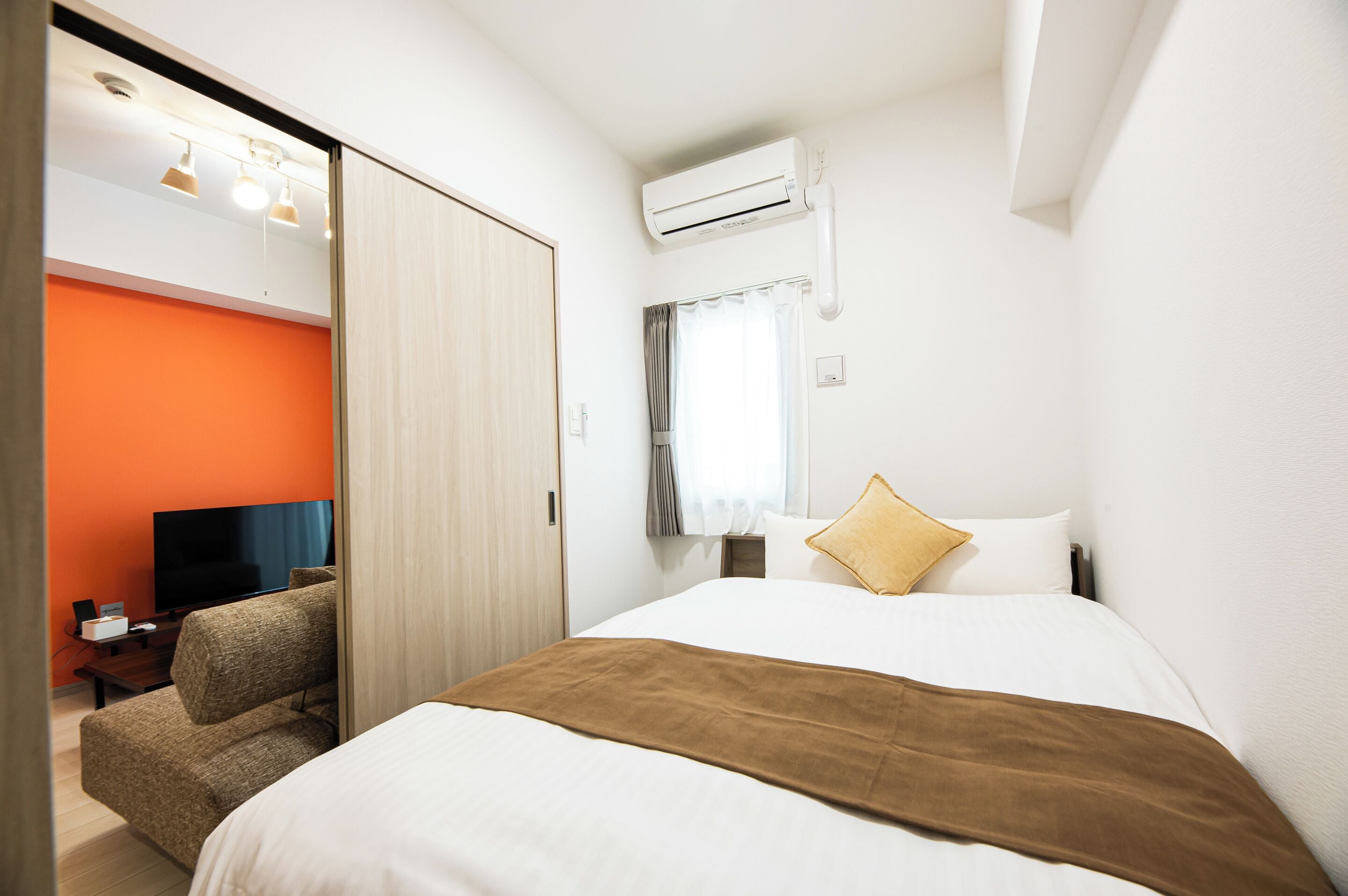 Una habitación de hotel con cama, televisor, escritorio y pared naranja.