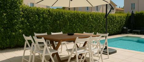 A poolside dining area with a table and chairs, an umbrella, and a pool.