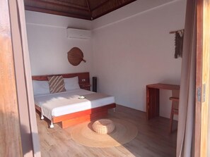 Ein Schlafzimmer mit einem Bett, einem Nachttisch, einem Sessel, einer gewebten Matte und einer Wanddekoration.