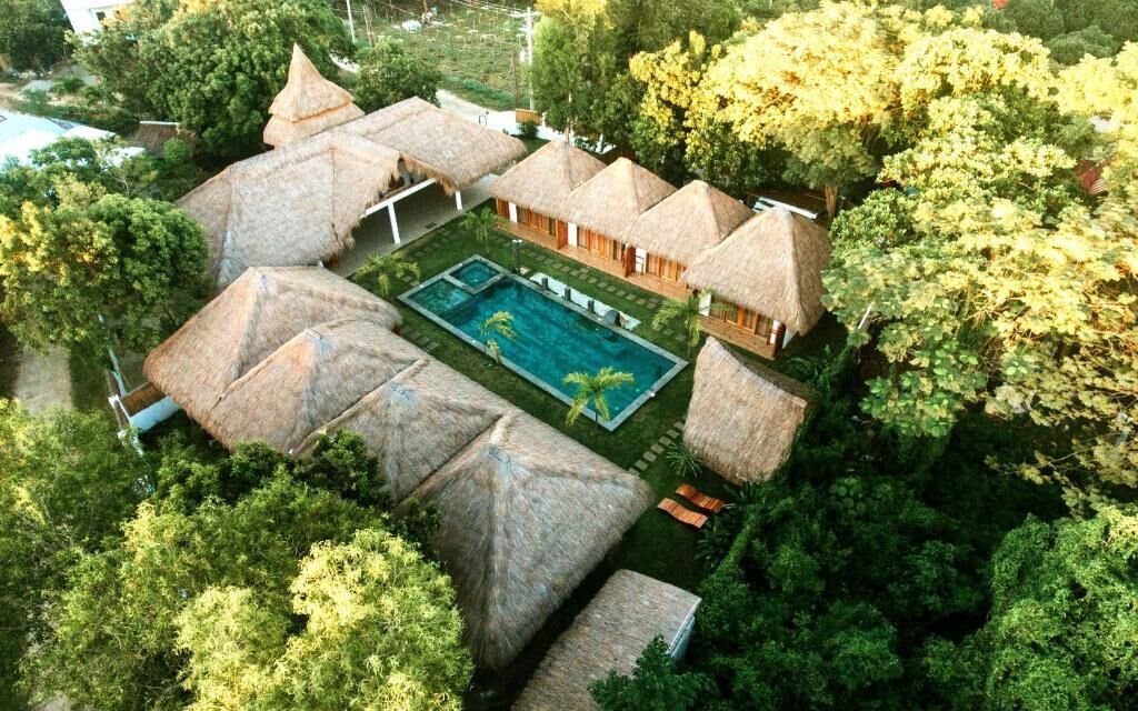 Un resort con villas de techo de paja, piscina y exuberante vegetación.