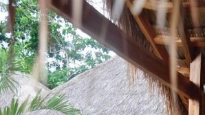 Estructura con techo de paja que incluye una cama y puertas de vidrio correderas, probablemente una habitación de huéspedes o suite privada.