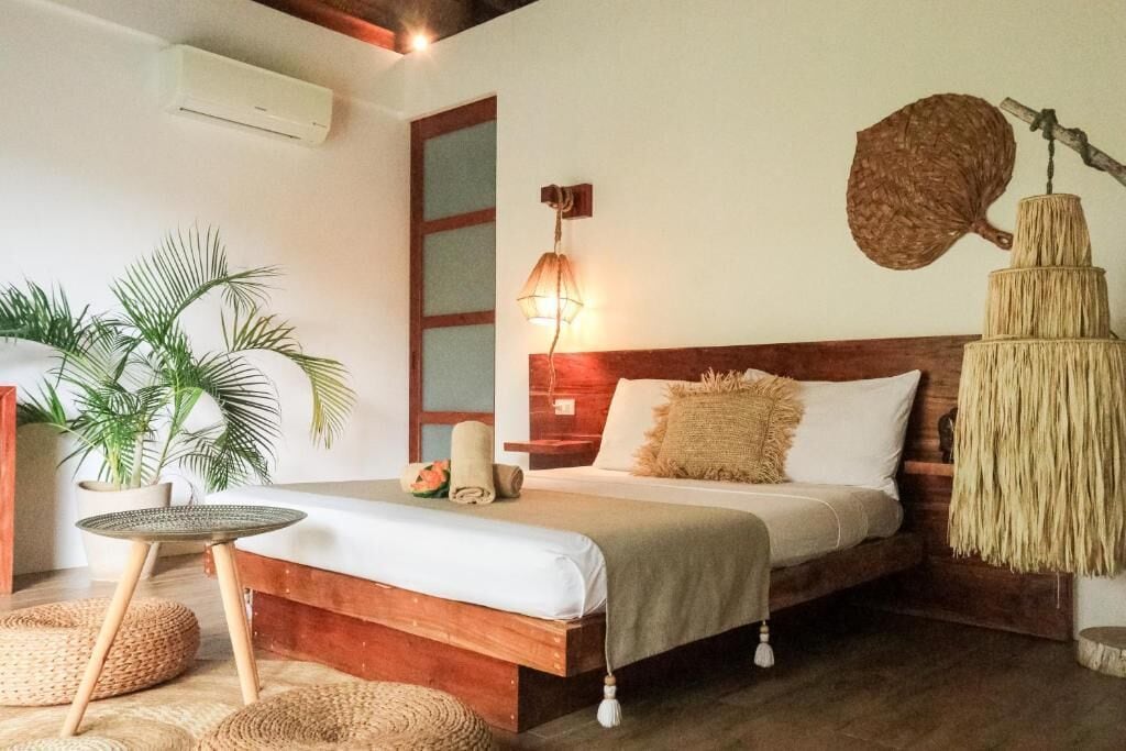 Un dormitorio con una cama de madera, una lámpara de noche, una cesta colgante tejida y una planta en maceta.