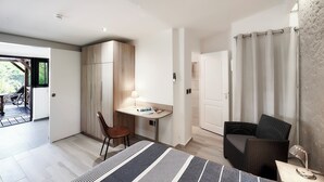 Et moderne værelse med et skrivebord, stol og en fletsofa. Der er en dør, der fører til et andet værelse, samt et vindue med gardiner.