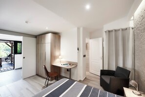 Ein modernes Zimmer mit Schreibtisch, Stuhl und einer Rattan-Couch. Eine Tür führt in einen anderen Raum und ein Fenster mit Vorhängen ist vorhanden.