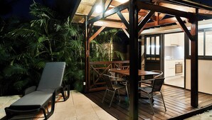 En udendørs terrasse med træterrasse, liggestol og et bord med stole.