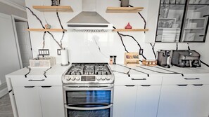 Et moderne køkken med hvide skabe, komfur i rustfrit stål og indbygget ovn.
