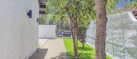 Un étroit sentier mène à un bâtiment à l’extérieur blanc, bordé d’arbres, sous un ciel dégagé.