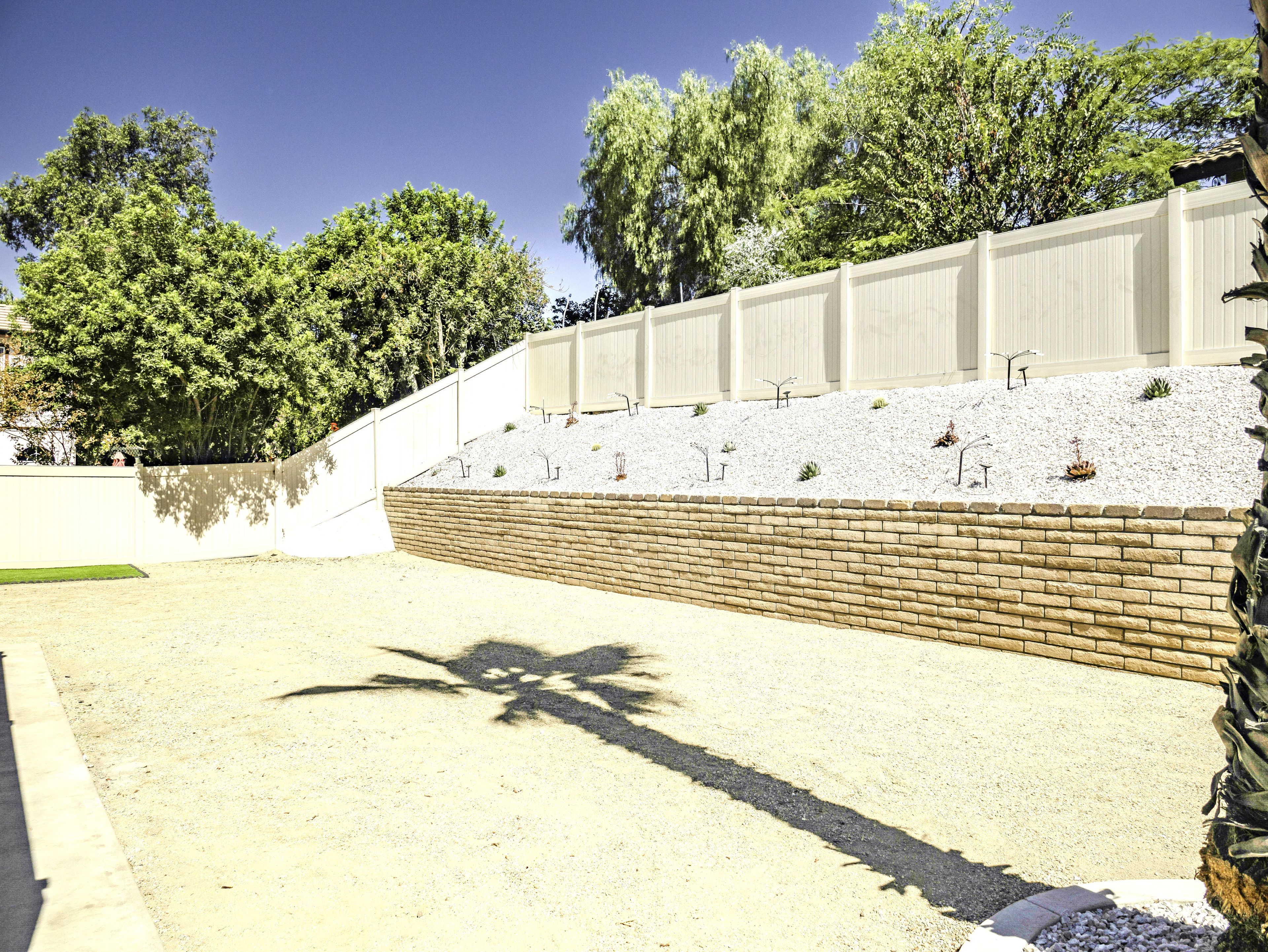 Un espace aménagé avec un mur de soutènement en briques, une clôture blanche et une variété de petites plantes.