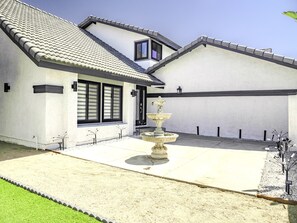 Una casa con techo de tejas, una puerta principal, ventanas y una fuente en el patio.