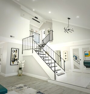 Un interior amplio con una escalera central, una lámpara moderna y una decoración de estilo minimalista.