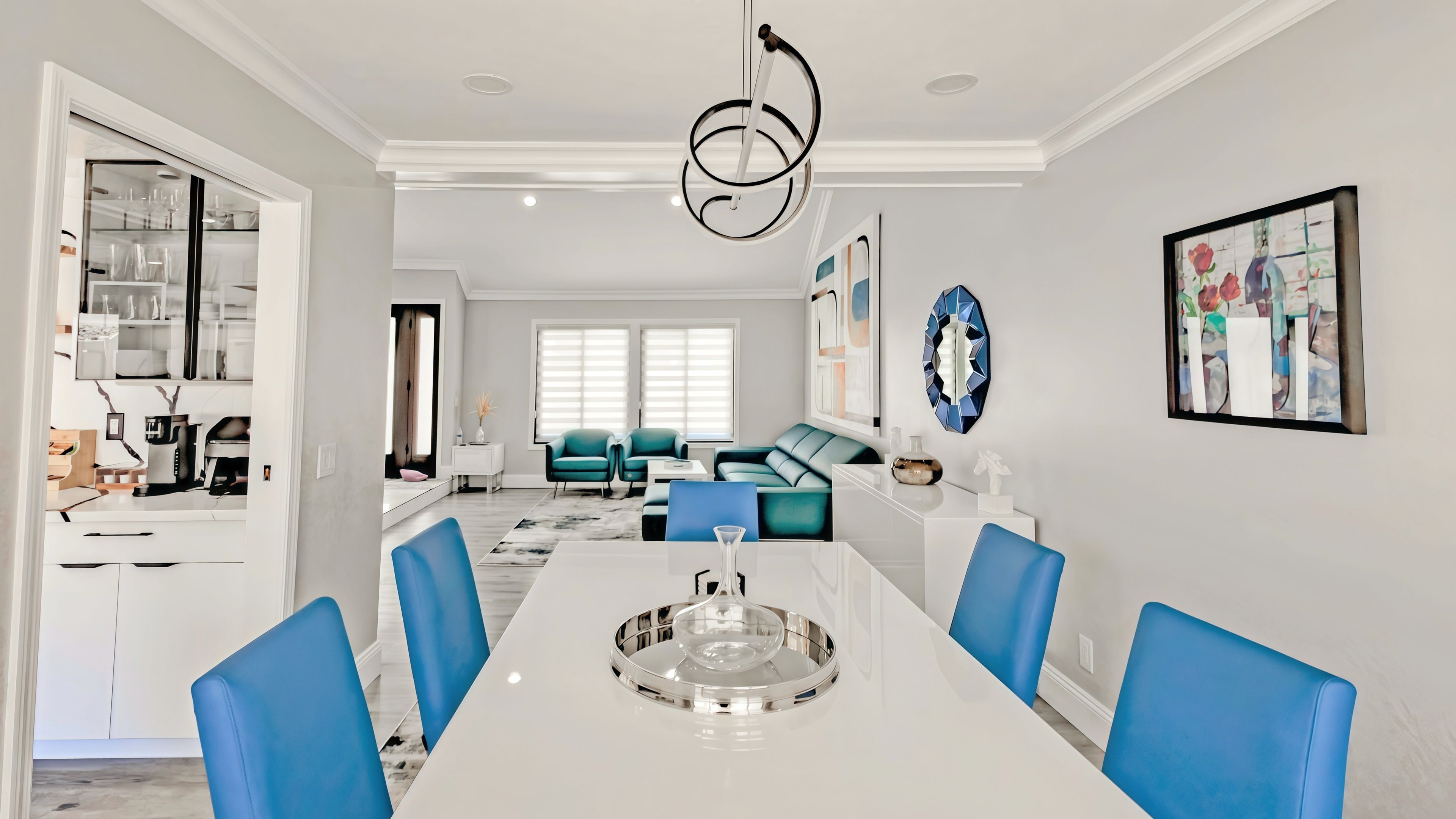 A modern dining area with a white table, blue chairs, and a unique chandelier.