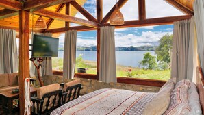 A room with a large bed, a desk, and a television. It has a view of a lake and hills. - The Best View in the Region, Private Beach, Cabin (Pet-Friendly) (Boyacá)