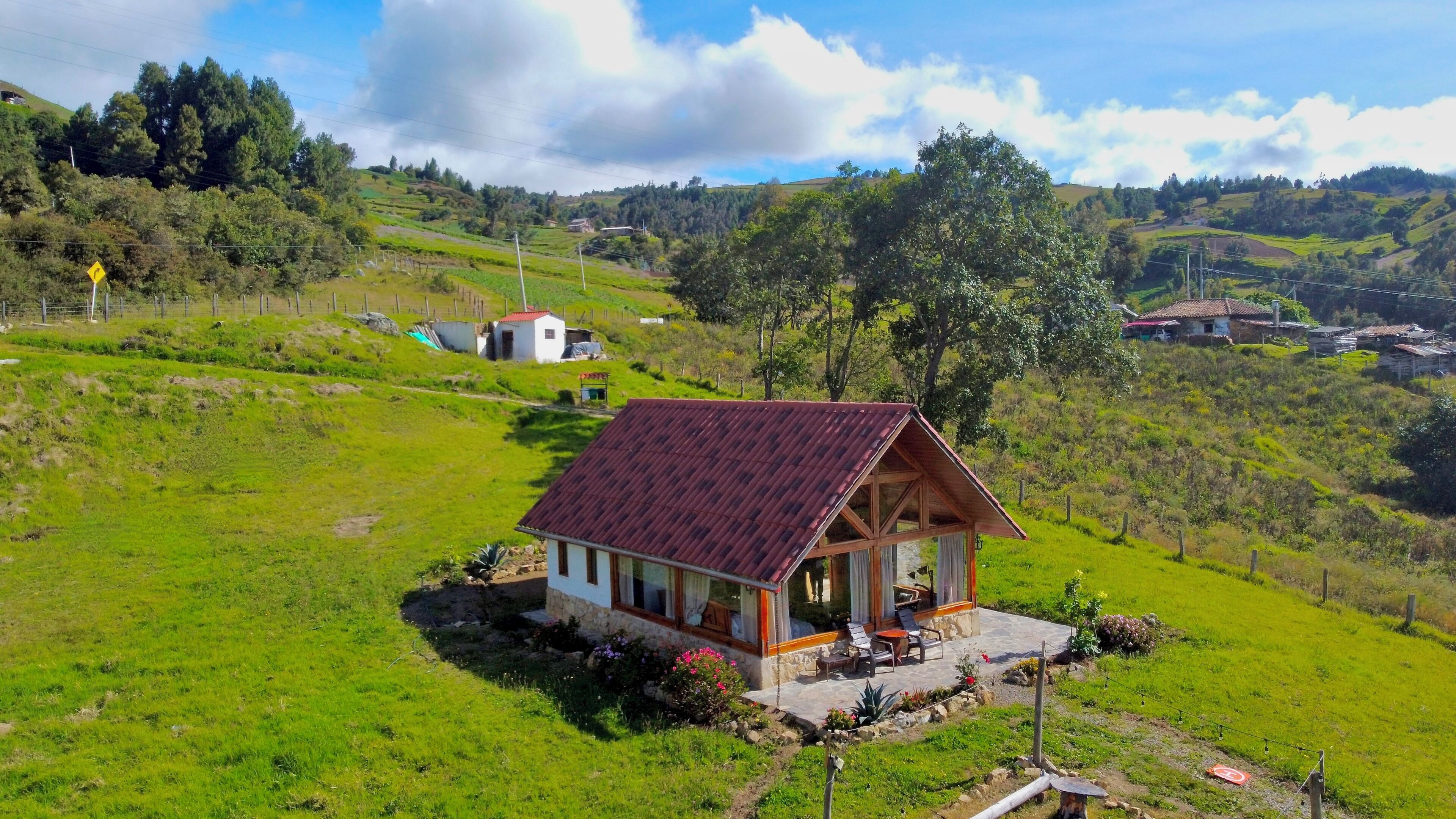 Une petite maison avec un toit rouge, une véranda avec des sièges et une vue sur le paysage verdoyant environnant.