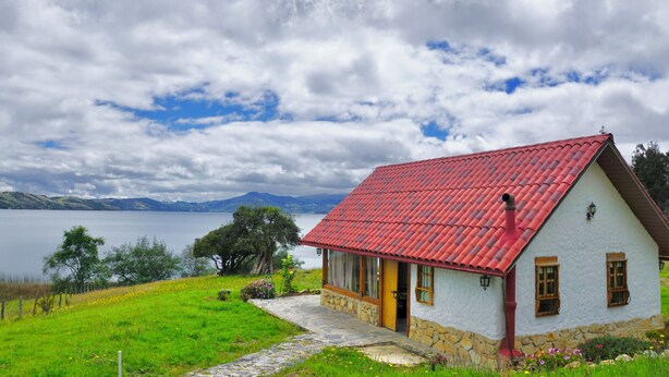 A house with a red roof, stone foundation, and a view of a lake and mountains in the background. - The Best View in the Region, Private Beach, Cabin (Pet-Friendly) (Boyacá)