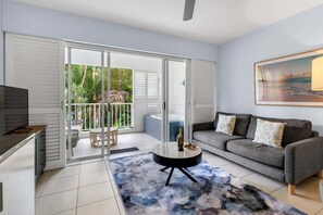 Ein modernes Wohnzimmer mit einem grauen Sofa, einem runden Couchtisch und einer Glastür zum Balkon.