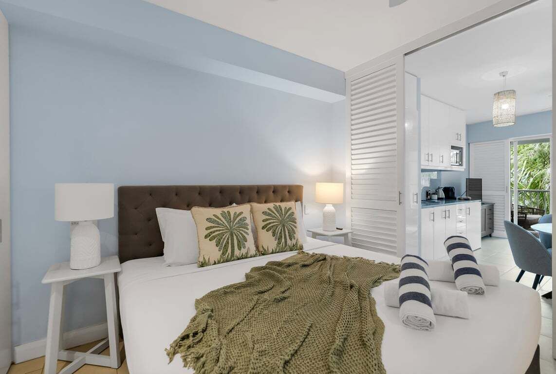 Una camera da letto con un letto, comodini, una lampada, una coperta e vista su un angolo cucina.