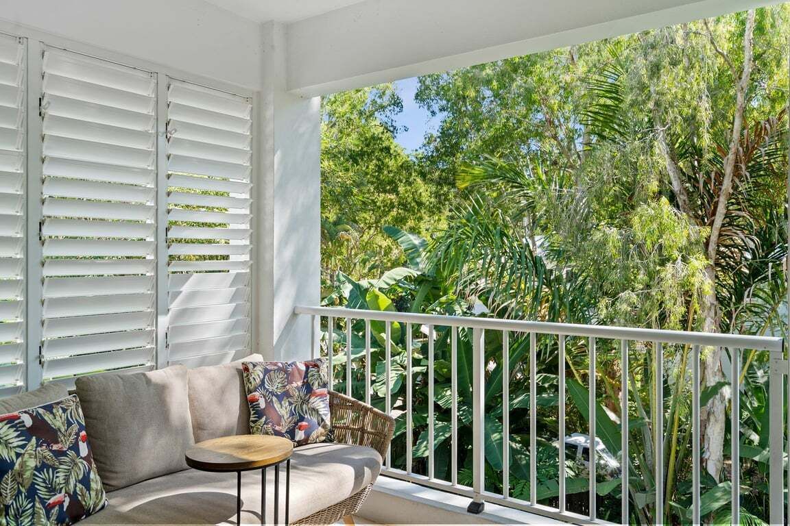 Ein Balkon mit weißer Brüstung, einer Couch mit Kissen und einem kleinen runden Tisch.