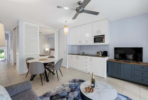 A modern kitchen with white cabinets, a microwave, and a television. There is a dining area with a round table and chairs. - 3434 Peppers Spa Penthouse (Palm Cove)