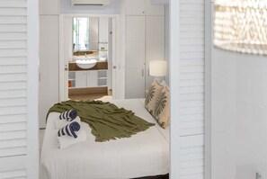 Ein Schlafzimmer mit einem Bett, einer Nachttischlampe und Blick ins Badezimmer.