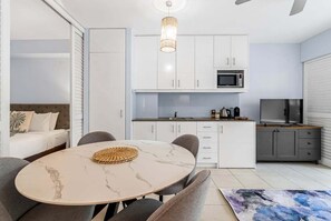 A modern kitchen with white cabinets, a microwave, and a dining area with a marble table and chairs. - 3434 Peppers Spa Penthouse (Palm Cove)