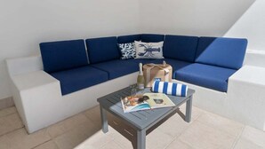A blue sofa with a white bench, a small table with a magazine, a bottle, and a striped pillow. - 3434 Peppers Spa Penthouse (Palm Cove)