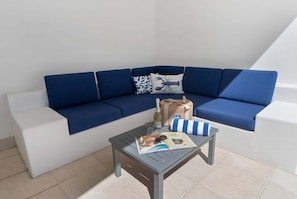 A blue sofa with a white bench, a small table with a magazine, a bottle, and a striped pillow. - 3434 Peppers Spa Penthouse (Palm Cove)