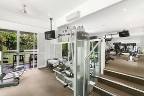 A gym with various exercise equipment, including a treadmill and weight machines, and a large window offering a view of the outdoors. - 3434 Peppers Spa Penthouse (Palm Cove)