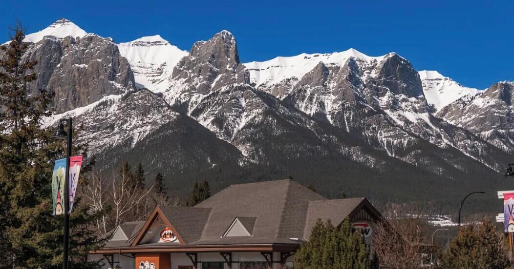 A mountain range with snow-capped peaks, a building with a sloped roof, and a clear blue sky.