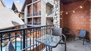A balcony with a glass table and chairs, a pool, and a stone wall. - Chic Twin Rockies Getaway - Pool&HotTub | Sleeps 8 (Canmore)