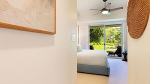 Ein Schlafzimmer mit einem Bett, einem Deckenventilator und Blick auf einen Garten durch eine Schiebetür.