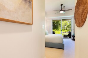 A bedroom with a bed, a ceiling fan, and a view of a garden through a sliding glass door. - The Islands at Mauna Lani - New Furnishings - Walk to beach and shops (Waimea)
