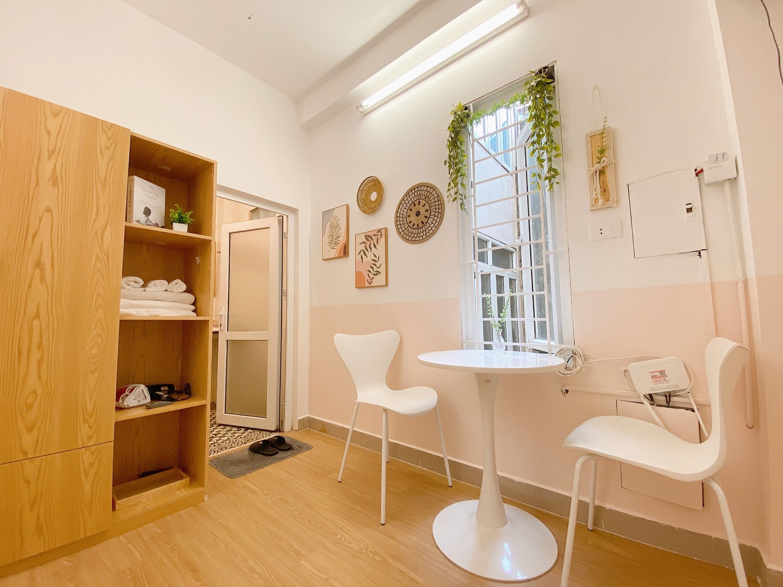 A modern room with a wooden wardrobe, a round table with two chairs, a window with greenery, and wall decorations.