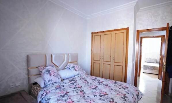 A bedroom with a bed, a wardrobe, and a door leading to another room. - Charming 2-bedroom Apartment With City View in Martil (Martil)