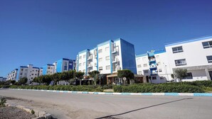 Une rangée d’immeubles résidentiels à plusieurs étages, dotés de balcons, un ciel dégagé et une route au premier plan.