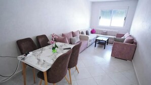 A modern living room with a dining area, featuring a marble table, brown chairs, and a sofa set. - Charming 2-bedroom Apartment With Garden View in Martil (Martil)