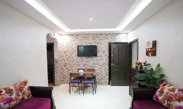 A living room with a TV mounted on the wall, a dining table with chairs, and two sofas. - Charming 2 -bedroom Apartment in Martil, Morocco (Martil)