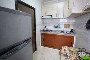 A kitchen with a refrigerator, wooden cabinets, a tiled backsplash, and a countertop with various kitchen items. - Charming 2 -bedroom Apartment in Martil, Morocco (Martil)