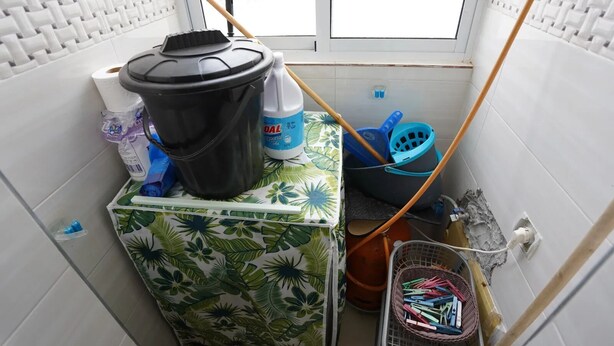 A small bathroom with a shower area, a toilet, and a sink. There is a window providing natural light, and various cleaning supplies are visible. - Charming 2 -bedroom Apartment in Martil, Morocco (Martil)