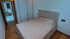 Ein Schlafzimmer mit einem Bett, Holzboden, einem Kleiderschrank und einer Tür zu einem weiteren Raum.