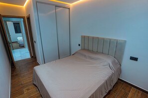 A bedroom with a bed, wooden flooring, a wardrobe, and a door leading to another room. - Charming 2-bedroom Apartment in the Heart of Martil, Morocco (Martil)