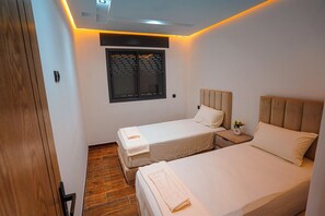 A bedroom with two beds, a window with blinds, a bedside table with a vase, and a wooden floor. - Charming 2-bedroom Apartment in the Heart of Martil, Morocco (Martil)