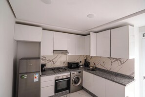 A compact kitchen with white cabinets, a stainless steel refrigerator, a microwave, a stove, and a washing machine. - Charming 2-bedroom Apartment in the Heart of Martil, Morocco (Martil)